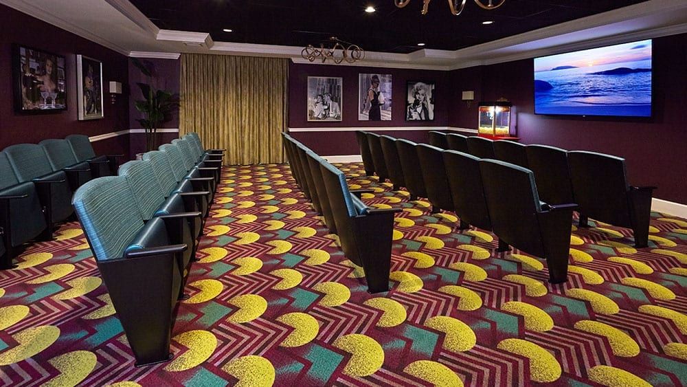 A vibrant and stylish theater room with colorful carpeting and rows of empty seats, adorned with classic movie posters on the walls.