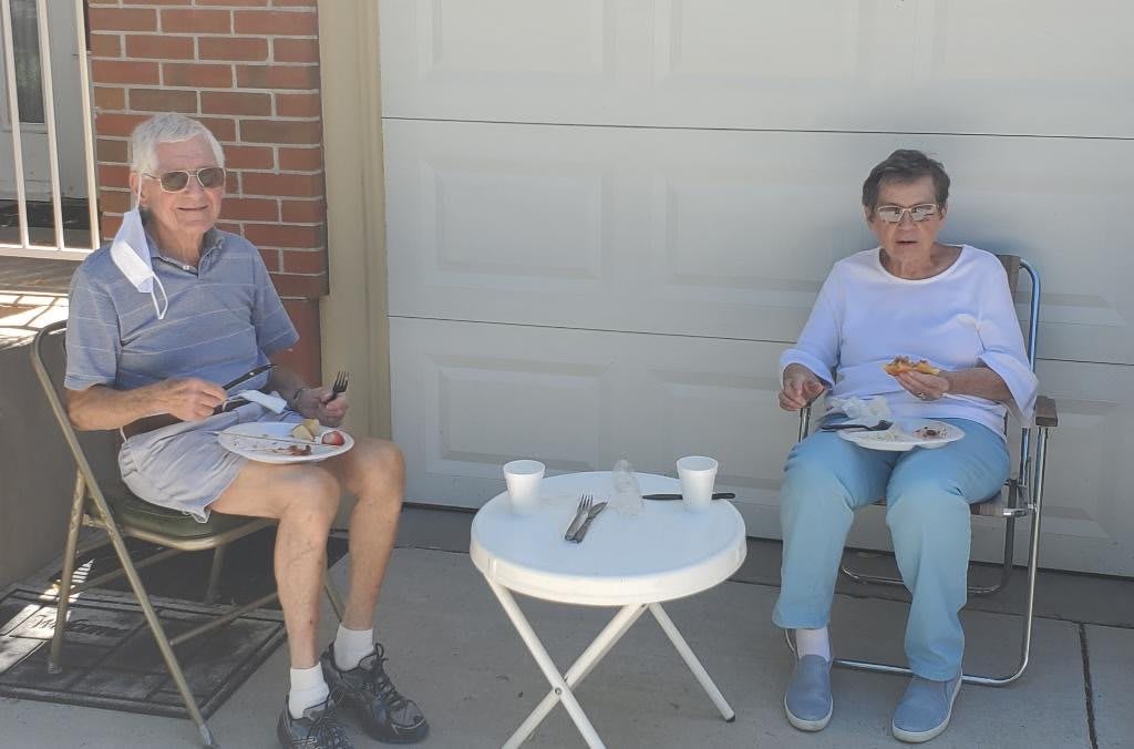 Two seniors enjoying a meal outdoors at a small table.