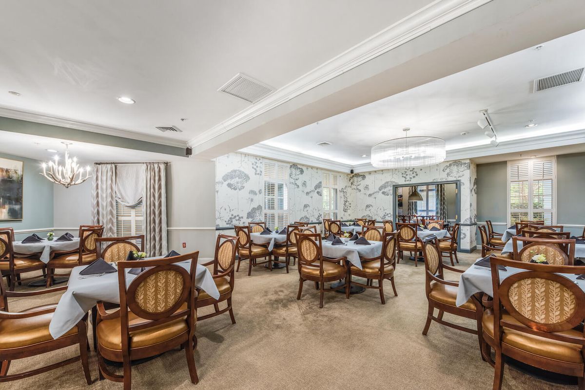 An elegantly designed dining room featuring classic wooden chairs, neatly arranged tables, and a central chandelier.