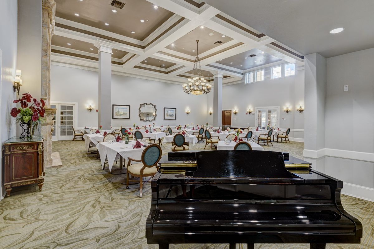 An elegant dining hall featuring a grand piano, decorated with chandeliers and neatly arranged tables and chairs.