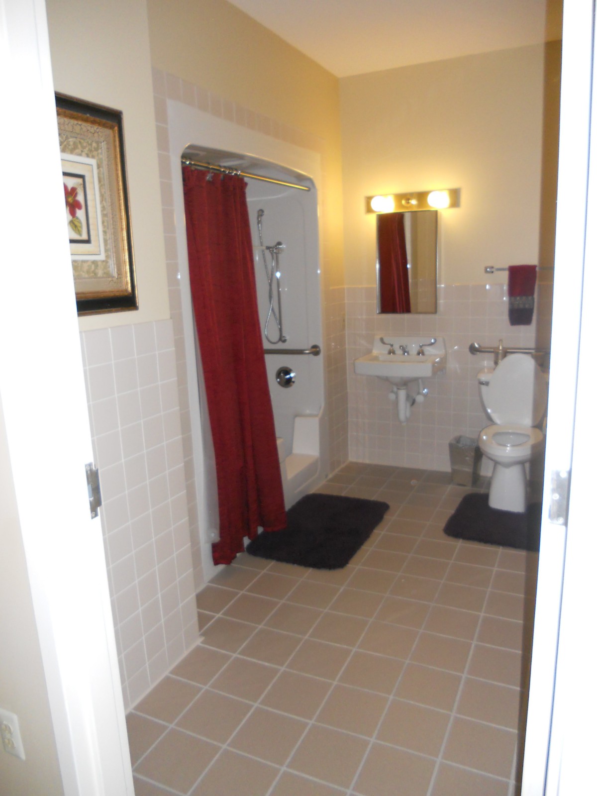 A clean bathroom featuring a shower with a red curtain, toilet, sink, and mirror.