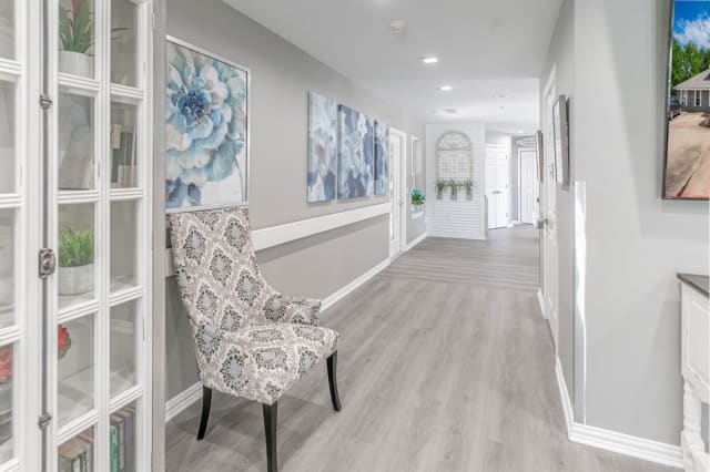 A modern, bright hallway featuring elegant artwork and a patterned chair against light-colored floors.