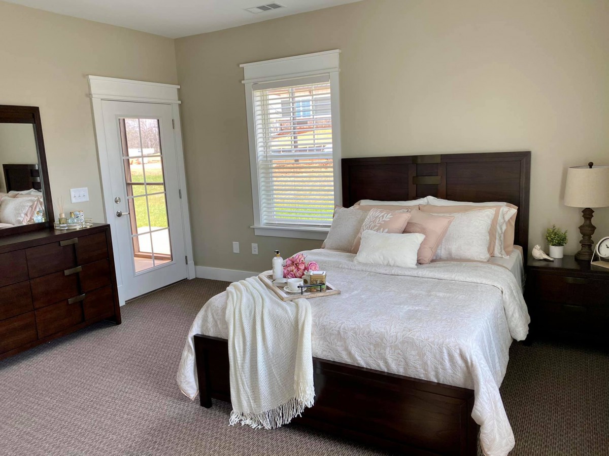 A cozy bedroom featuring a neatly made bed with decorative pillows and a throw blanket, complemented by ample natural light from the windows.