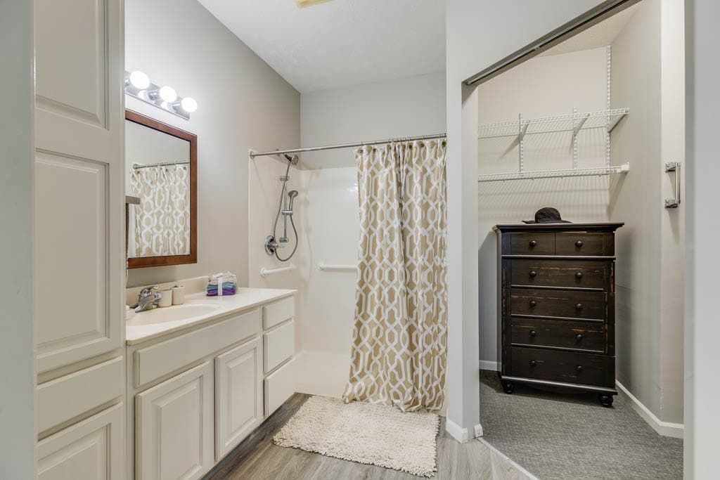 A modern bathroom with a shower, vanity, and an adjacent walk-in closet.