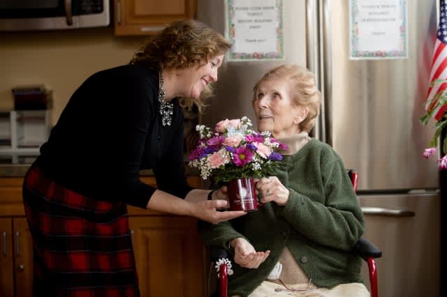 A younger woman presents flowers to an elderly woman in a caring gesture.