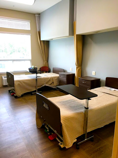 A view of a shared patient room in a hospital, featuring two beds and natural light coming through the window.