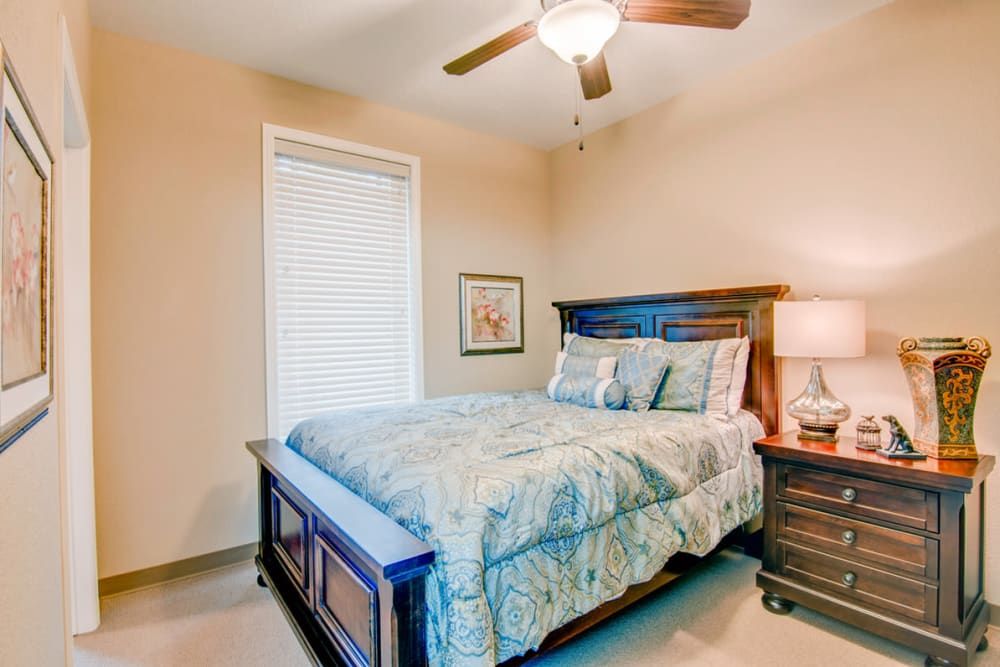 A cozy bedroom with a bed, nightstand, lamp, and ceiling fan.