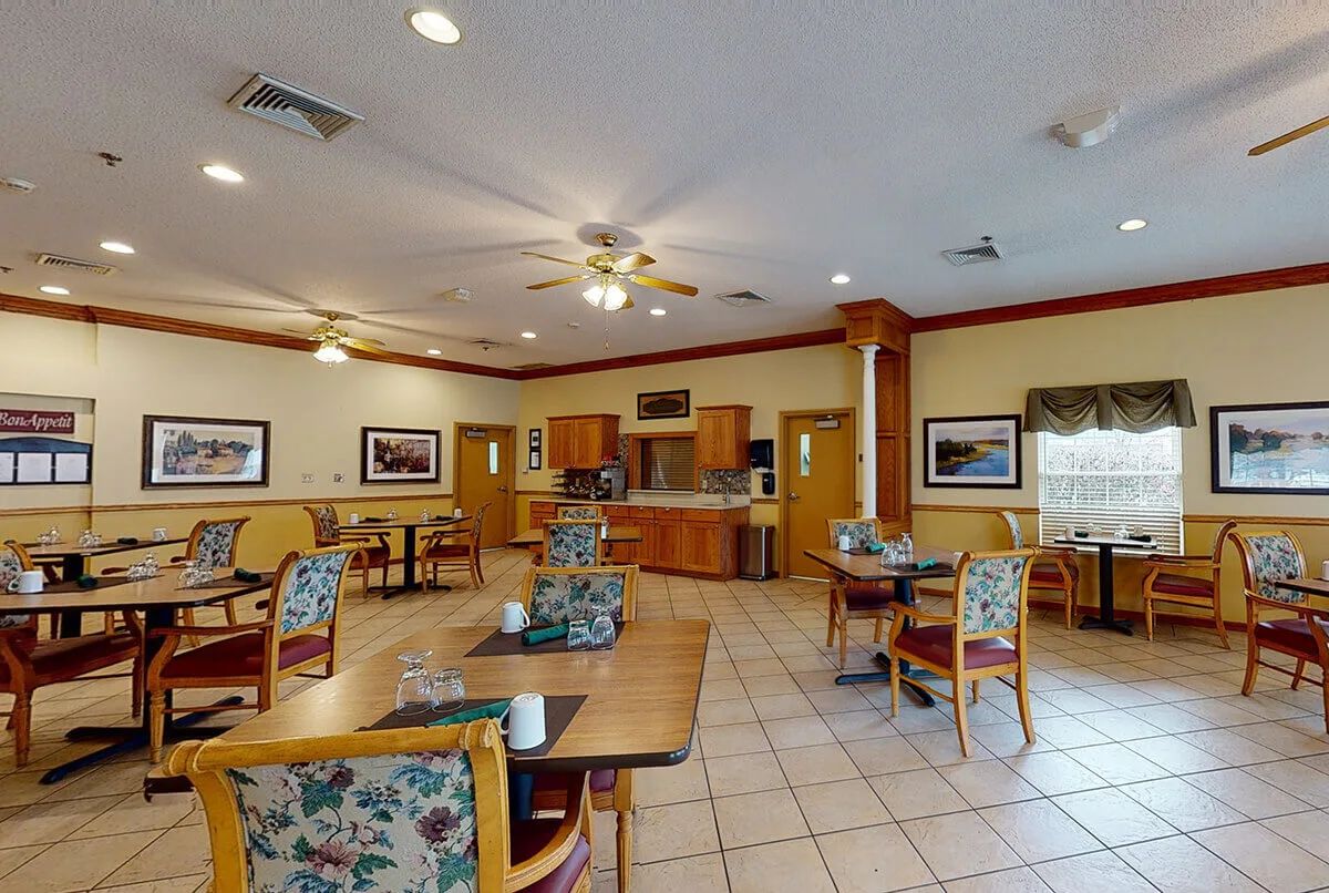 An indoor dining area with neatly arranged tables and chairs, featuring warm lighting and framed artwork on the walls.