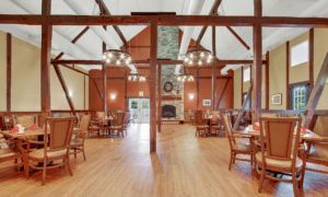 A rustic dining area featuring wooden beams, chandeliers, and a stone fireplace.