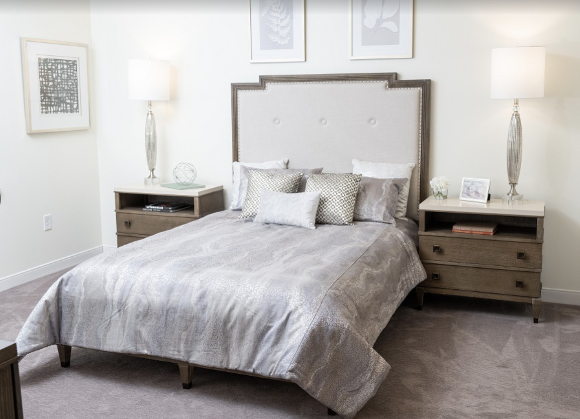 A cozy and elegantly designed bedroom featuring a comfortable bed with soft gray bedding, flanked by wooden nightstands and contemporary lamps.