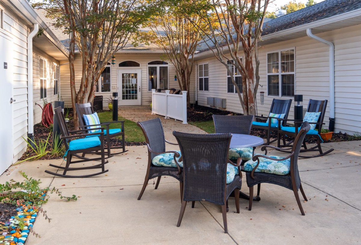 A cozy outdoor patio area with chairs and a table, surrounded by trees and greenery.