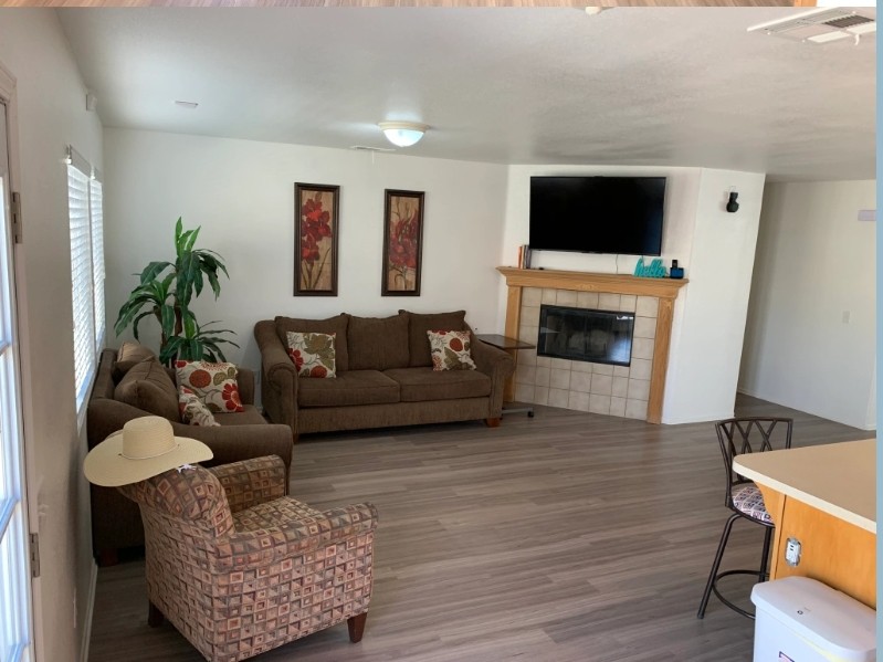 A cozy living room featuring a sofa, armchair, and television above a fireplace with wood flooring and wall art.