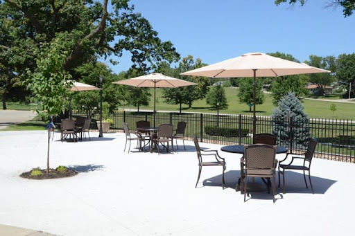 A tranquil outdoor seating area featuring tables and umbrellas, surrounded by lush greenery.