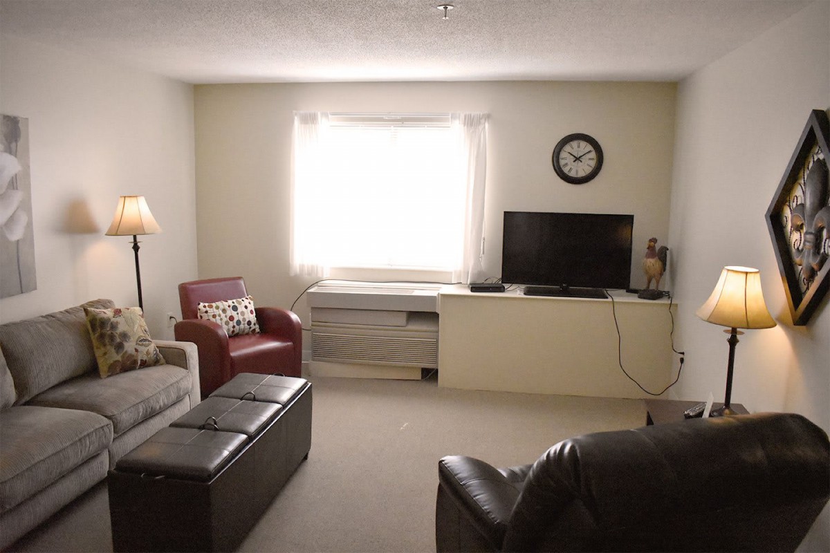 A cozy living room with a sofa, armchair, television, and a clock on the wall.