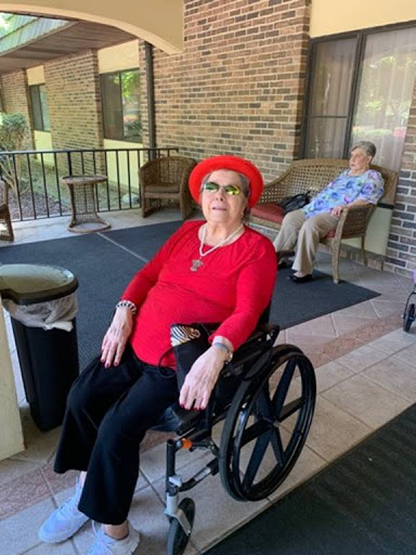 A cheerful elderly woman in a red outfit and hat enjoys her time outdoors in a wheelchair.