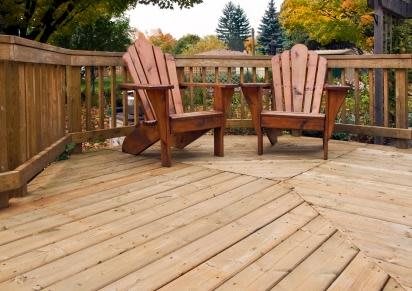 A wooden deck with two Adirondack chairs, surrounded by autumn foliage.