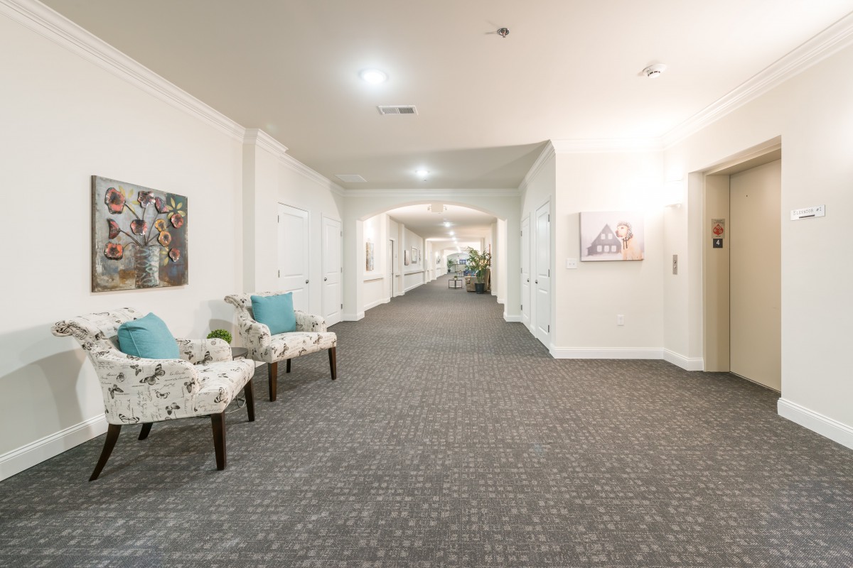 A well-lit hallway with floral chairs and wall art, featuring a carpeted floor.