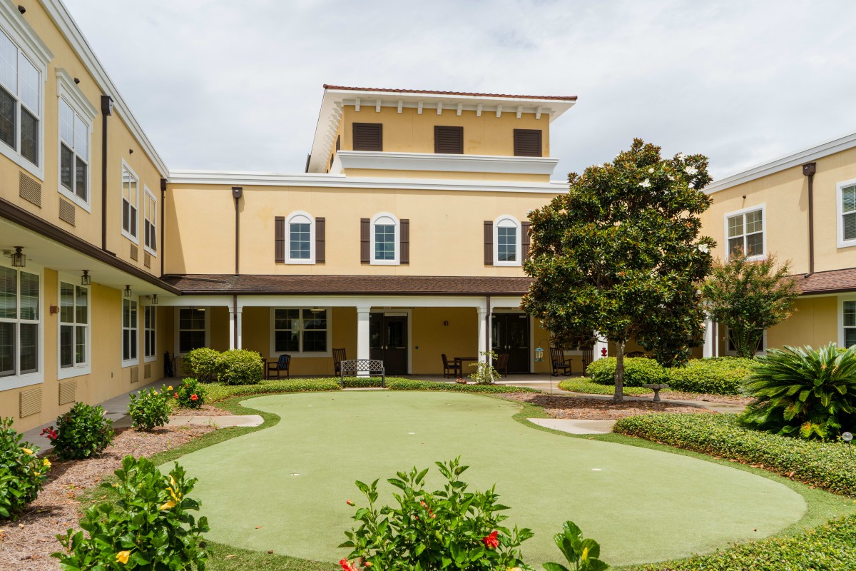 A view of a two-story building with a well-maintained garden and trees in the foreground.