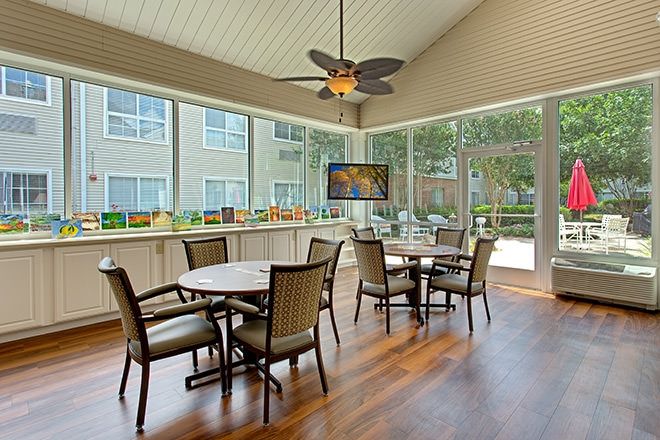 A modern dining area with tables and chairs, featuring large windows and a ceiling fan.