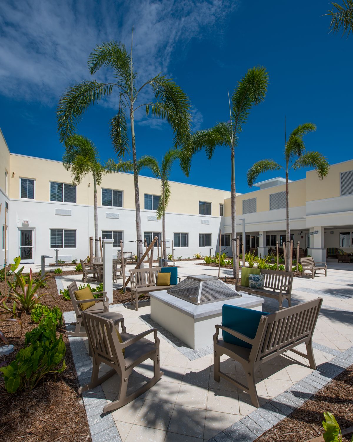 A modern courtyard with outdoor seating, palm trees, and stylish architecture under a clear blue sky.