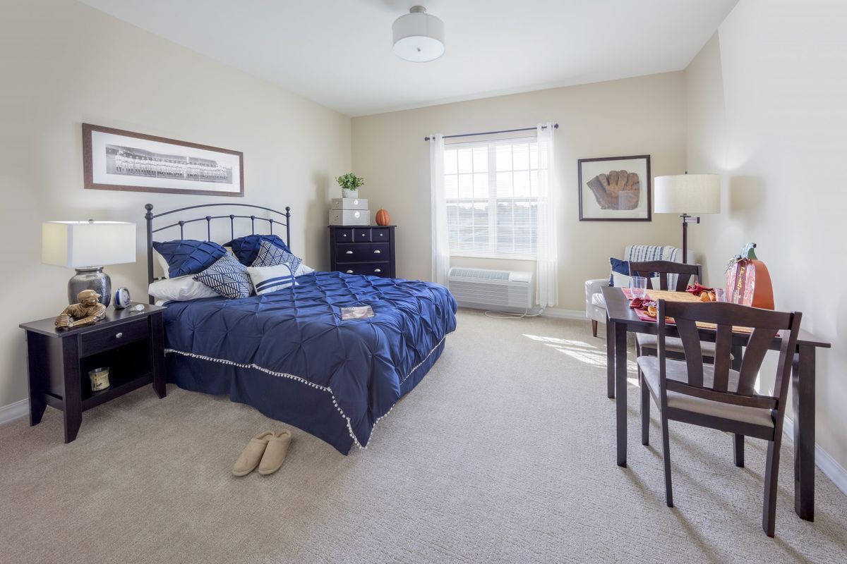 A cozy bedroom with a blue bedspread, light-colored walls, and a large window letting in natural light.