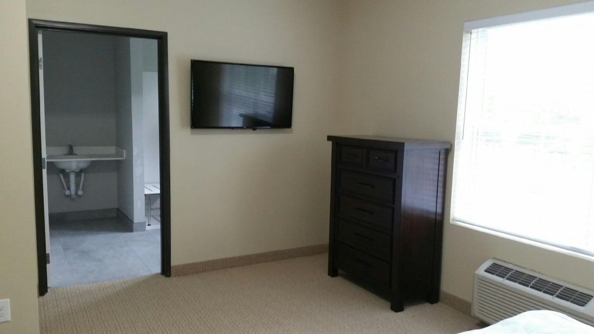 A minimalist bedroom featuring a wall-mounted television and a dark dresser.
