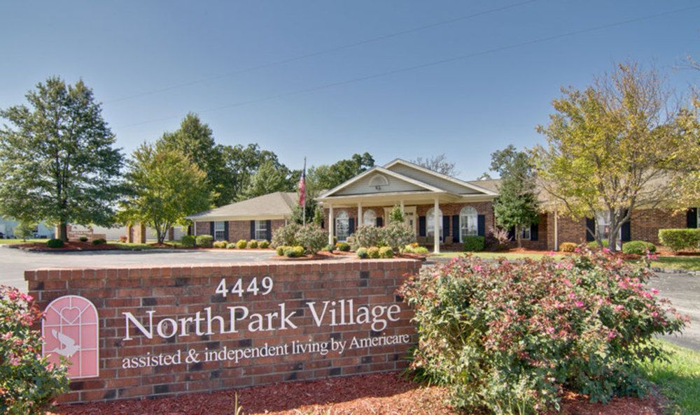 Entrance sign for NorthPark Village, an assisted and independent living facility, with a view of the main building and landscaped surroundings.