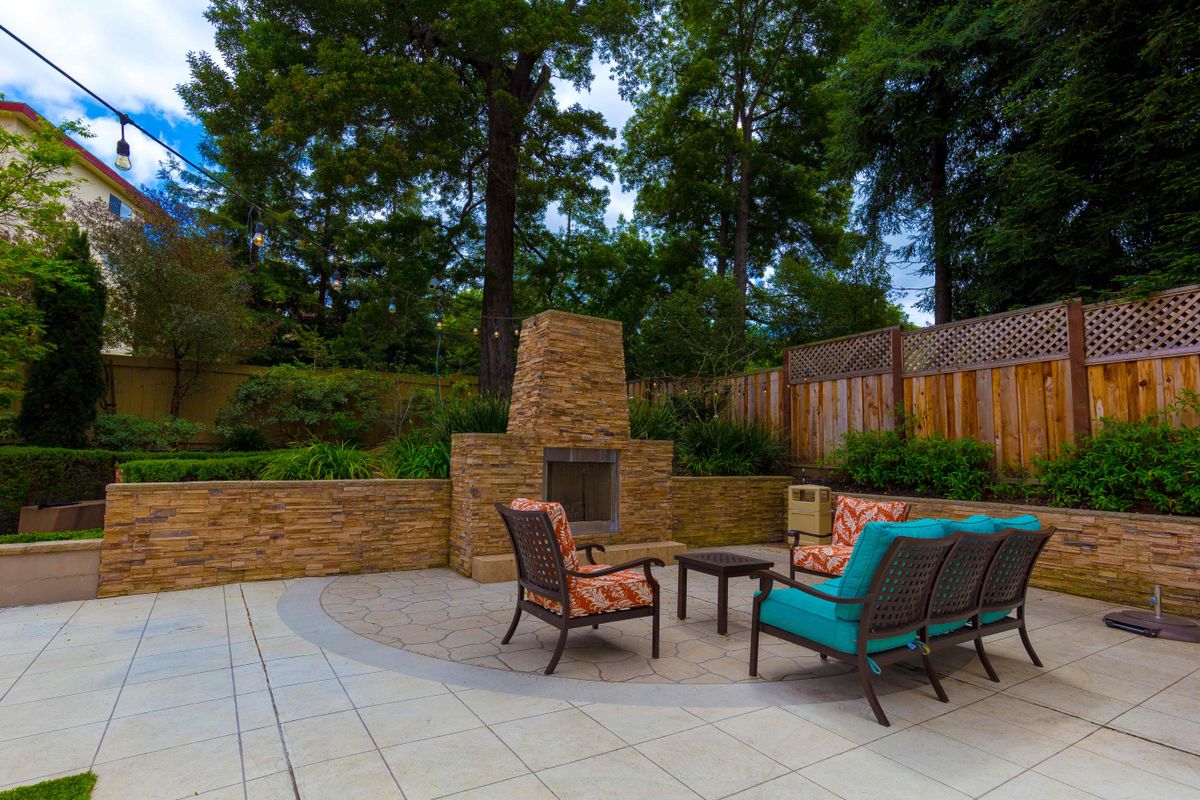A cozy outdoor patio with comfortable seating and a stone fireplace surrounded by greenery.