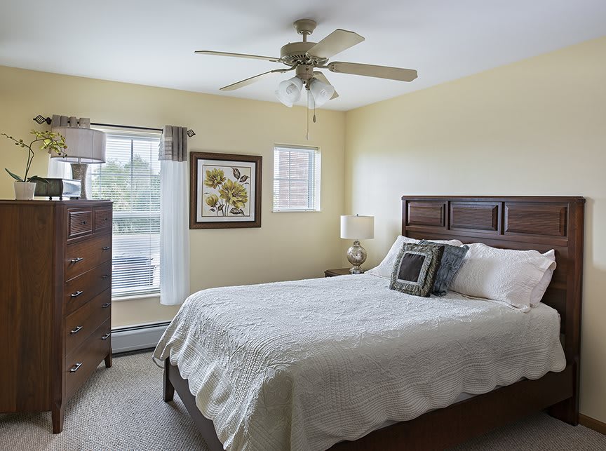 A cozy bedroom with a bed, ceiling fan, and natural light.
