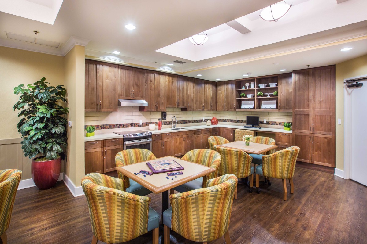 A modern kitchen and dining area with wooden cabinets, round tables, and upholstered chairs.