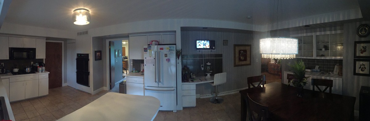 A modern kitchen with a refrigerator, desk, and wall-mounted TV.