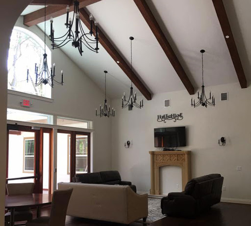 A spacious living room featuring elegant chandeliers and wooden beams, designed to maximize natural light.