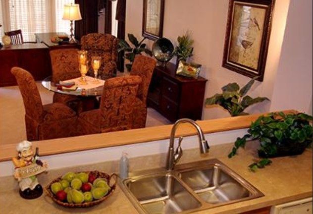 A cozy kitchen view with a double sink and a dining area in the background, featuring warm lighting and elegant decor.