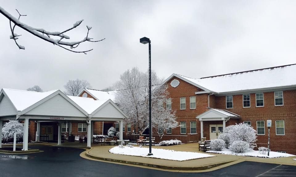 A snowy winter scene featuring a brick building and leafless trees under an overcast sky.
