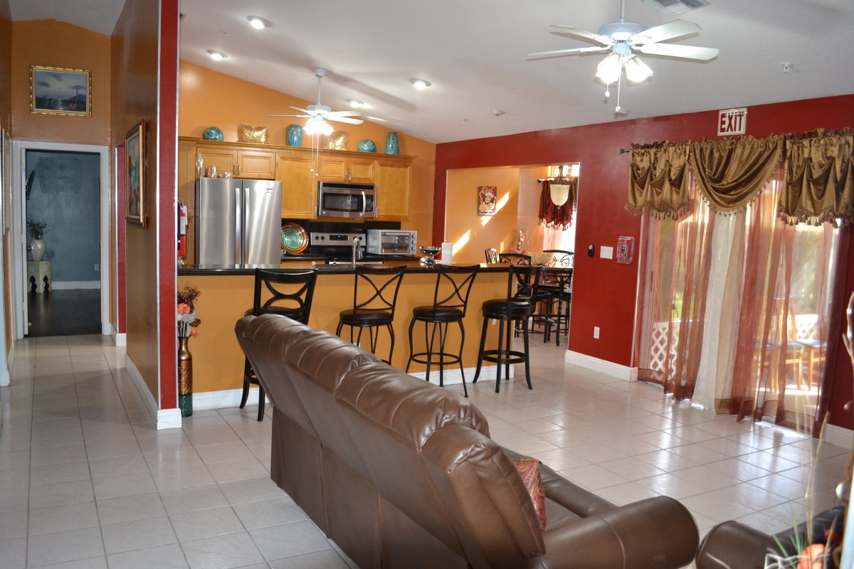 An open-concept kitchen and living room with colorful walls, featuring a seating area with bar stools, modern appliances, and a leather sofa.