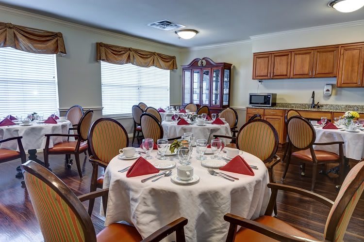 A cozy dining room with elegantly set tables and a view of the kitchen cabinets.