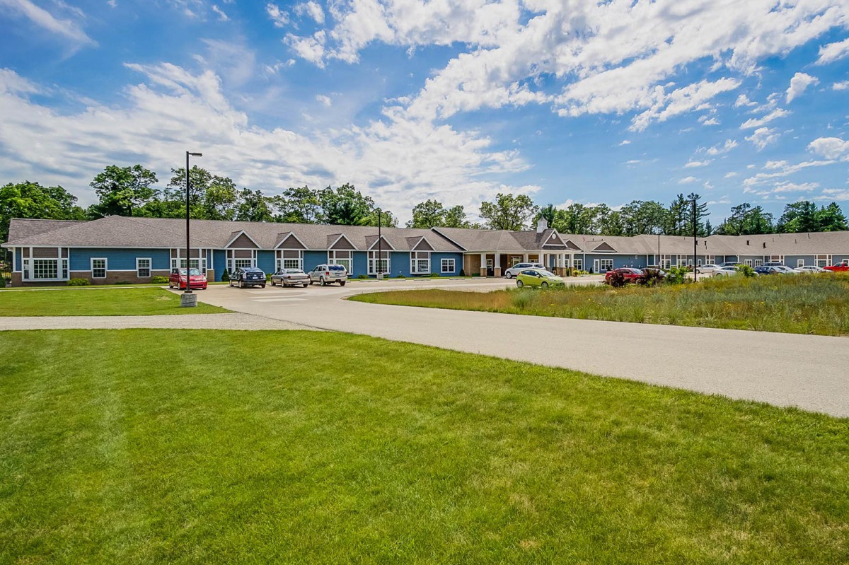 A scenic view of a residential building surrounded by a well-maintained lawn under a partly cloudy sky.