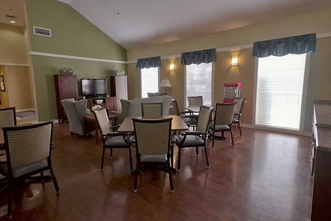 A cozy living and dining area with tables and chairs, featuring large windows and warm lighting.