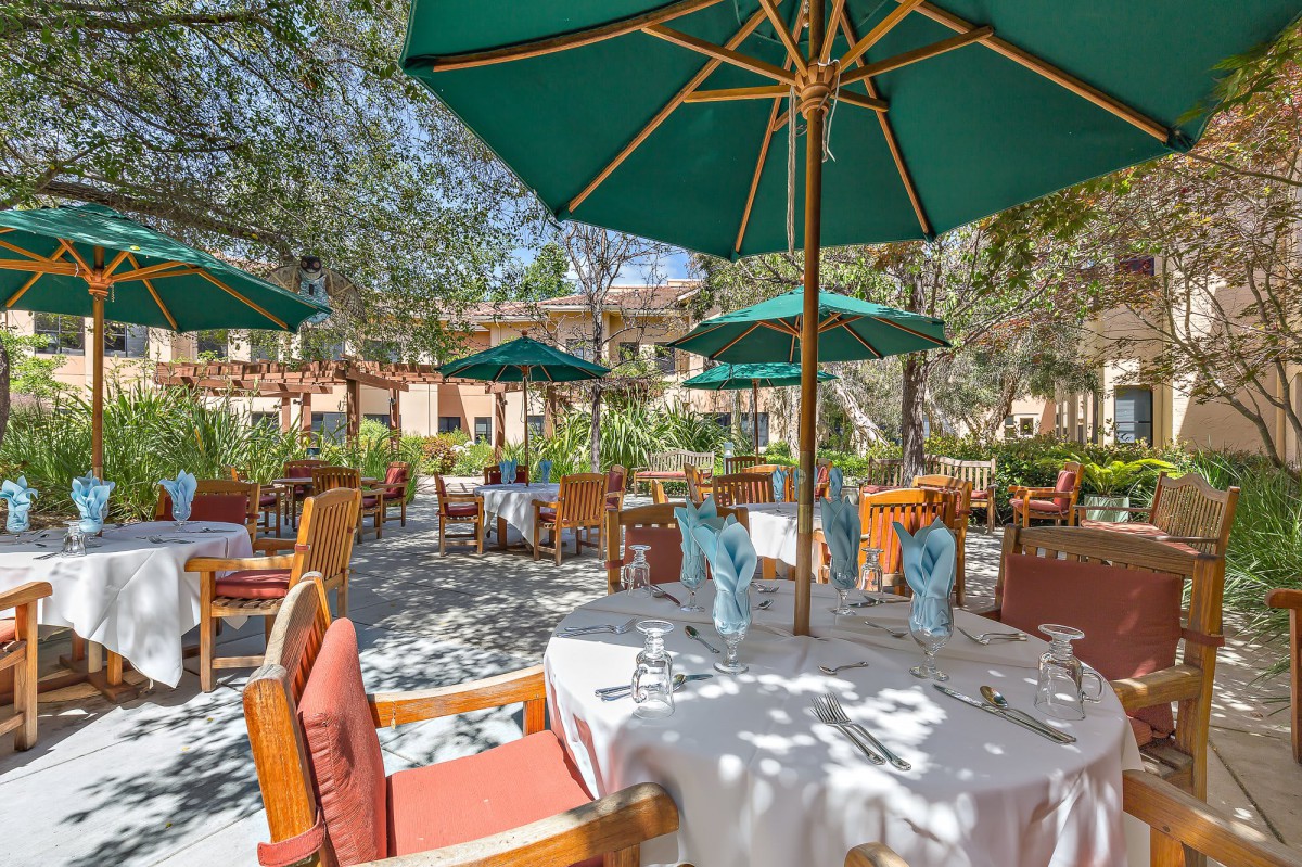An inviting outdoor restaurant patio with tables set for dining under large green umbrellas.