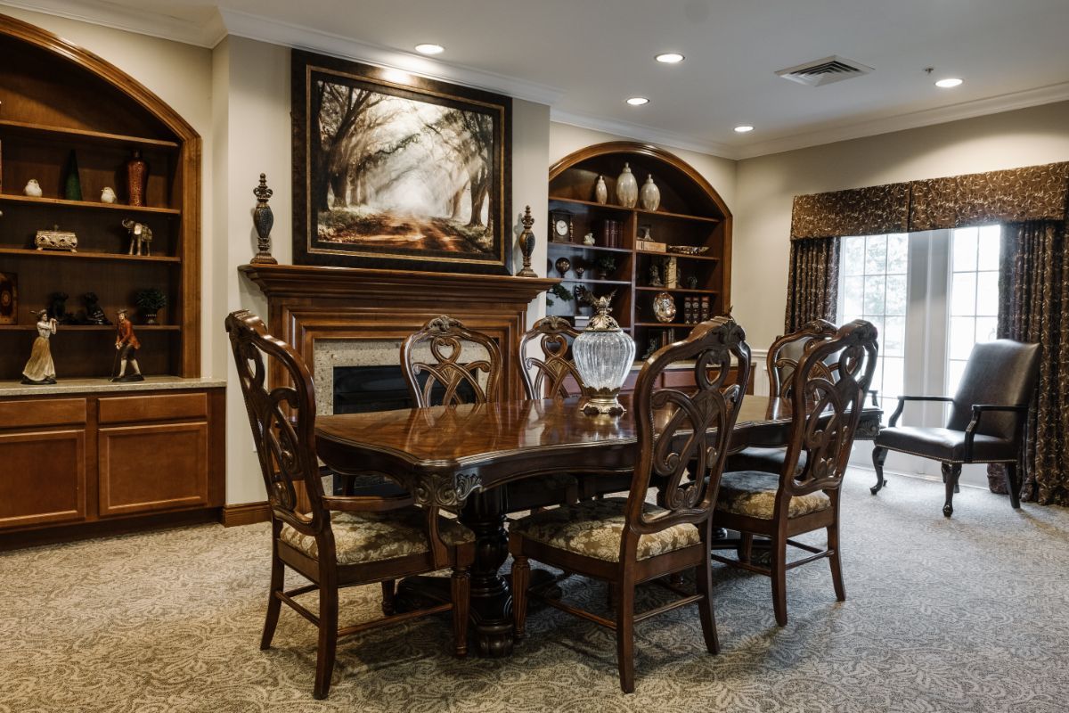 A beautifully furnished dining room with a large wooden table, ornate chairs, a fireplace, and artwork above the mantel.