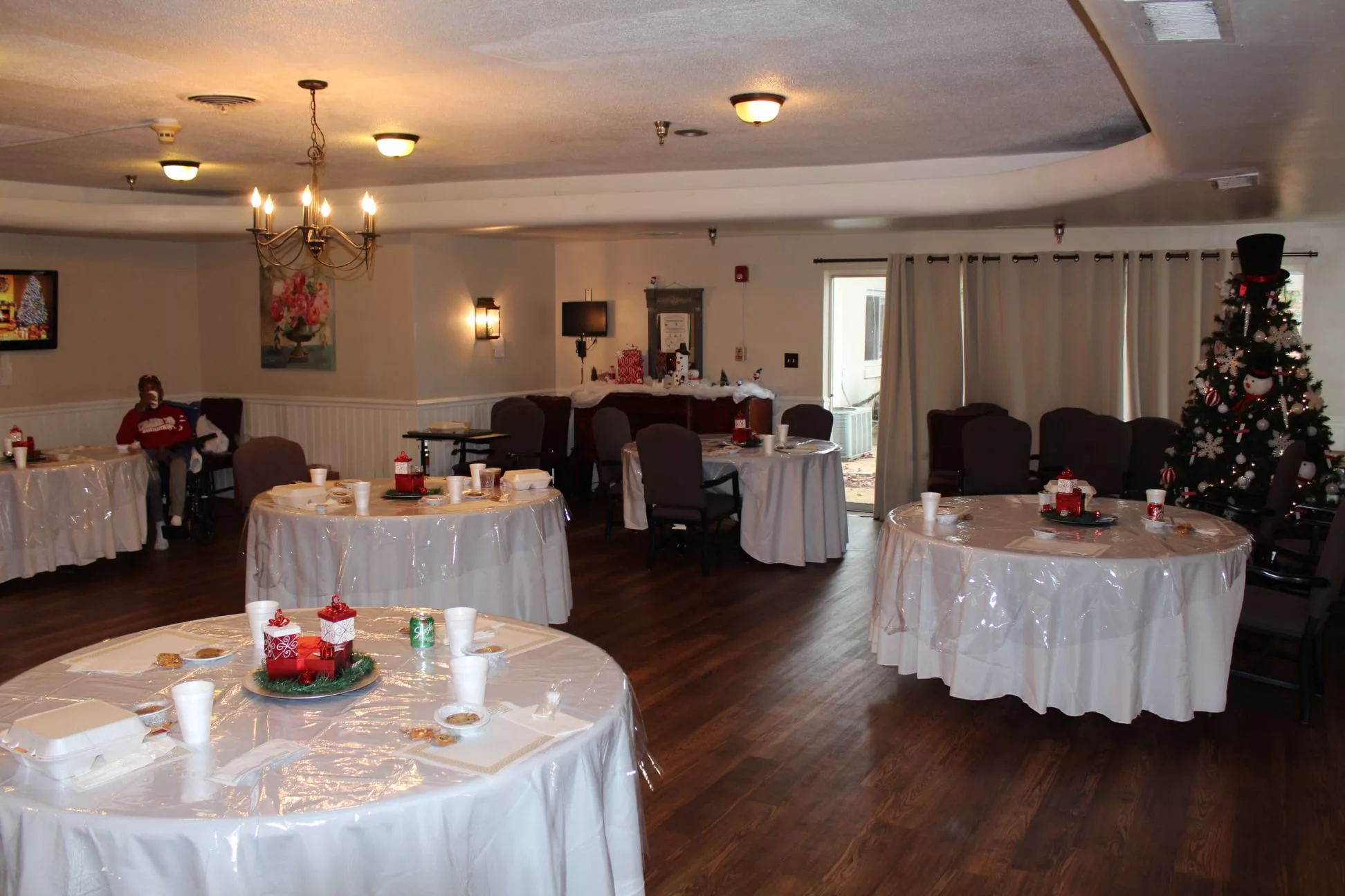 A decorated event space with round tables, chairs, and chandeliers.