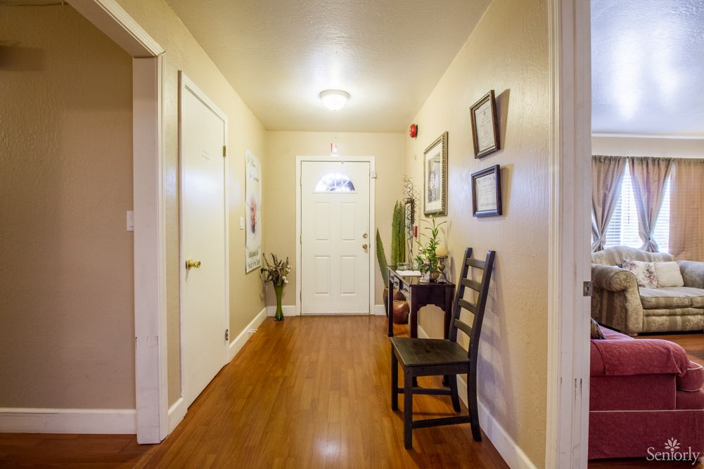 A warmly lit home hallway with wooden flooring, decorated with chairs, wall art, and plants.