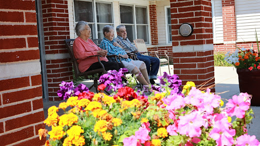 Three elderly individuals enjoy the outdoors on a sunny day, surrounded by vibrant flowers.