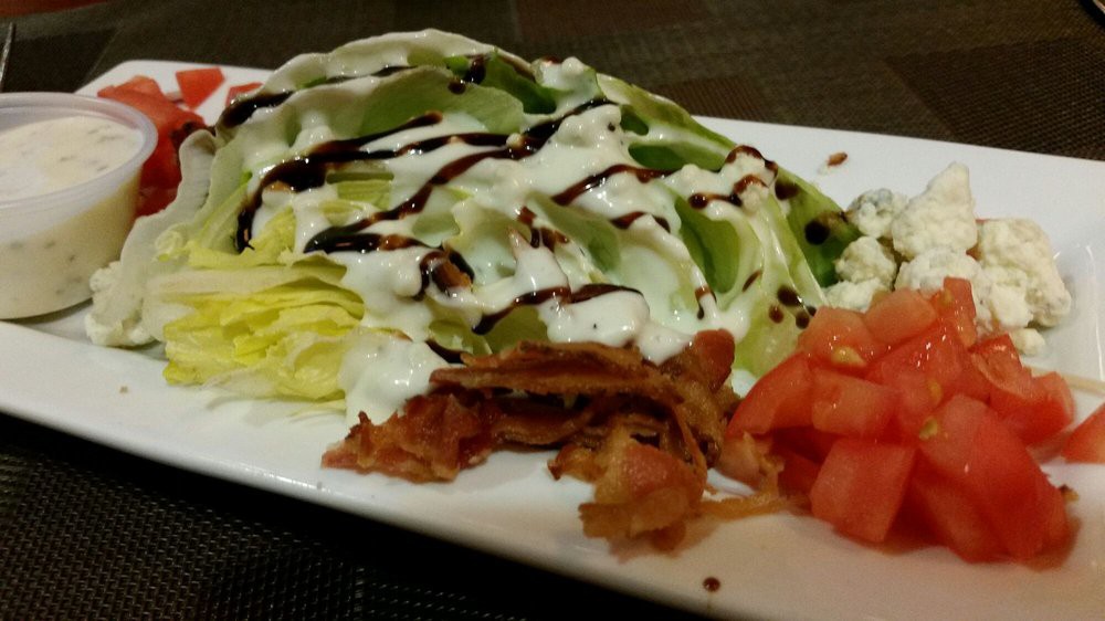 A wedge salad topped with creamy dressing, bacon, and sliced tomatoes.