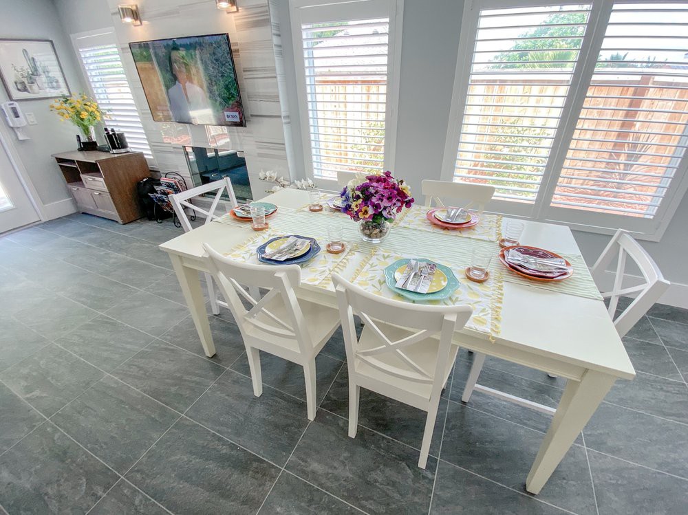 A bright and modern dining room featuring a white table set with colorful plates and a floral centerpiece.