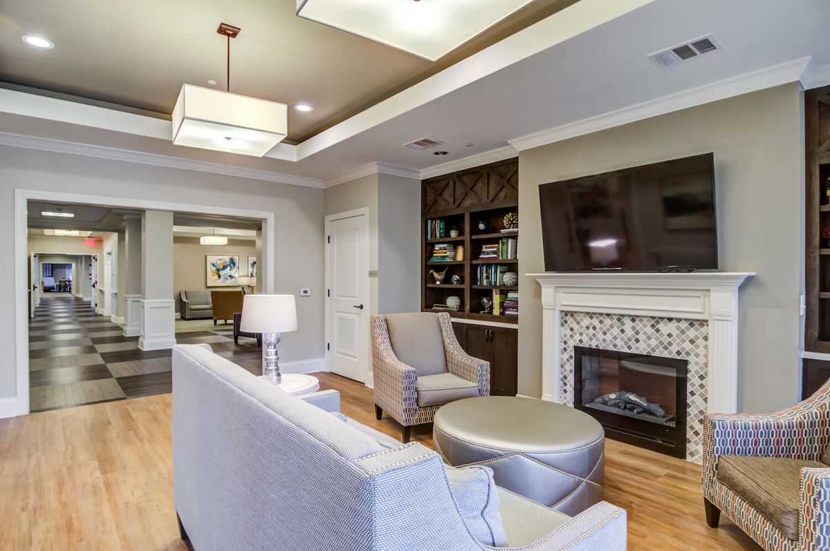 A modern living room featuring a cozy seating area with a sofa and armchairs, a television mounted above the fireplace, and a well-stocked bookshelf.