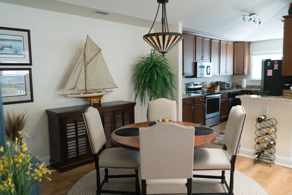 A cozy dining area with a round table and chairs, featuring a sailboat model on the sideboard and connected to a modern kitchen.