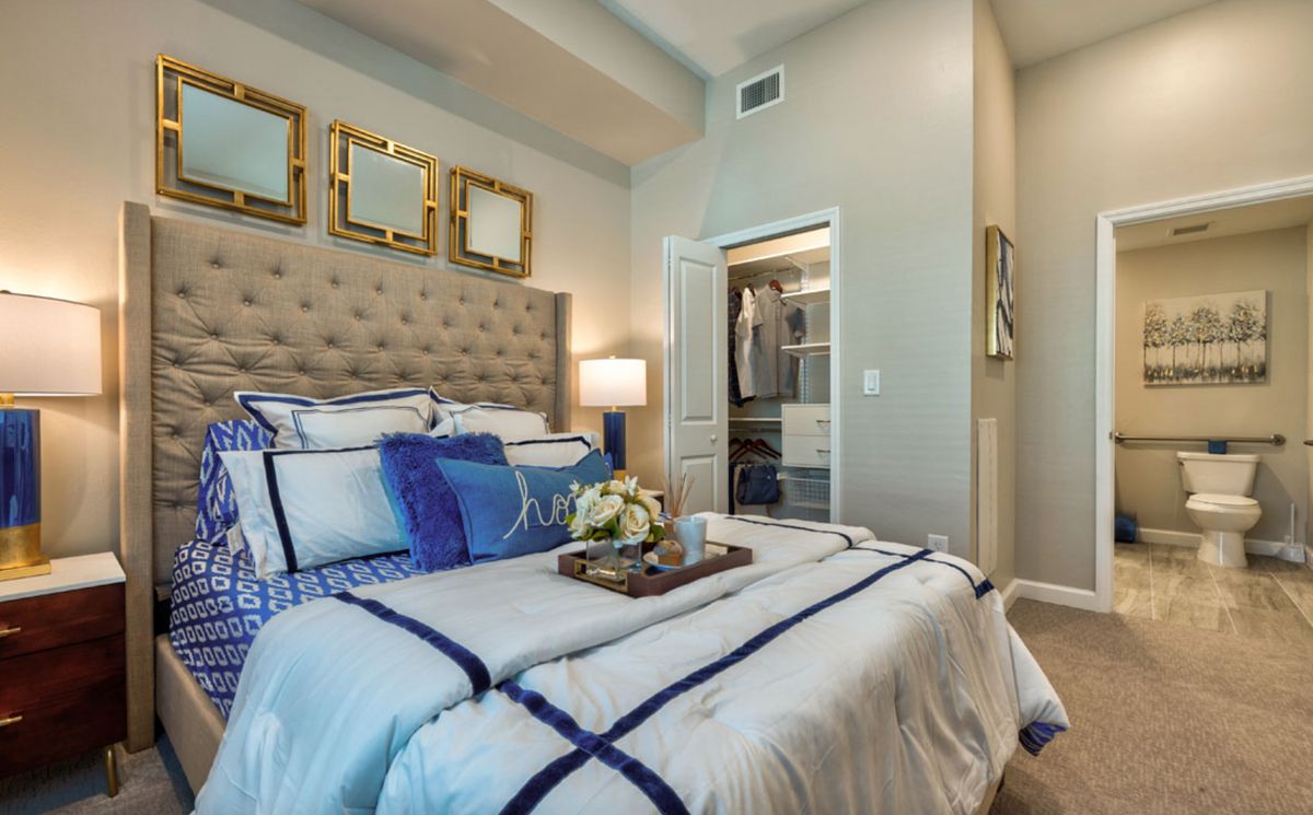 A modern bedroom with elegant decor, featuring a plush bed with blue and white bedding, complemented by stylish wall art and ambient lighting.