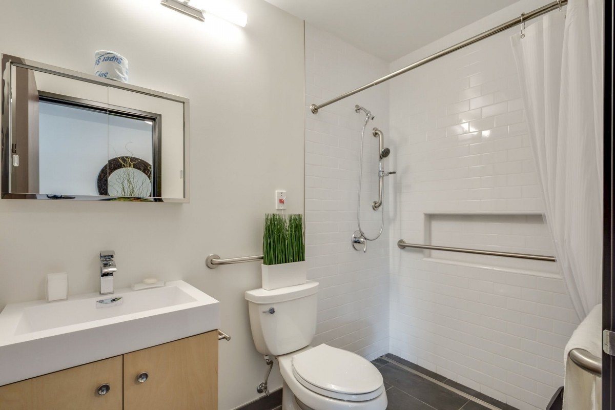 A modern, minimalist bathroom with a sink, toilet, and accessible shower.