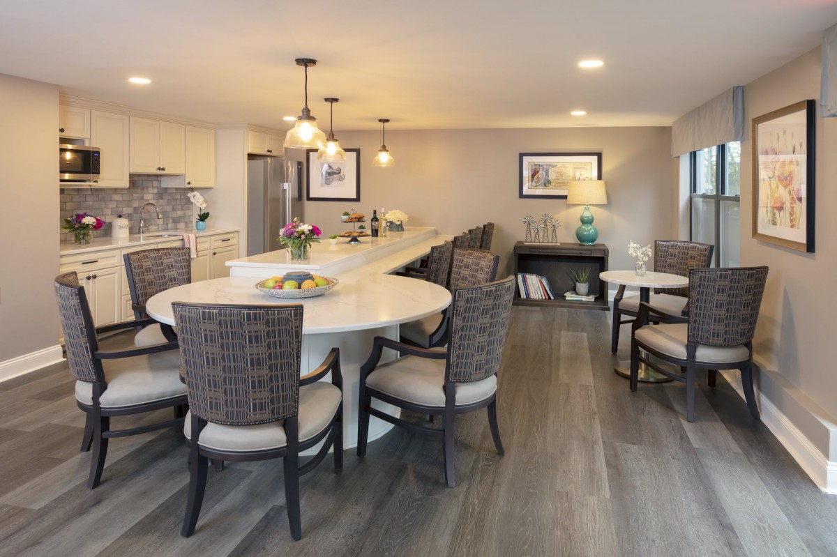 A modern open-concept kitchen and dining area featuring a round table with wicker chairs, pendant lighting, and wood flooring.